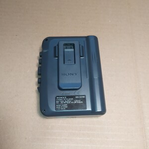 May include: A blue Sony WM-EX190 cassette player with a black belt clip. The player has a CE mark and the text "SONY CASSETTE PLAYER BATTERY SUPPLY 1.5V x 2 EC, JIS R6 SIZE AA OR EQUIV. SONY CORP. MADE IN CHINA 3-042-294-01" printed on the back.