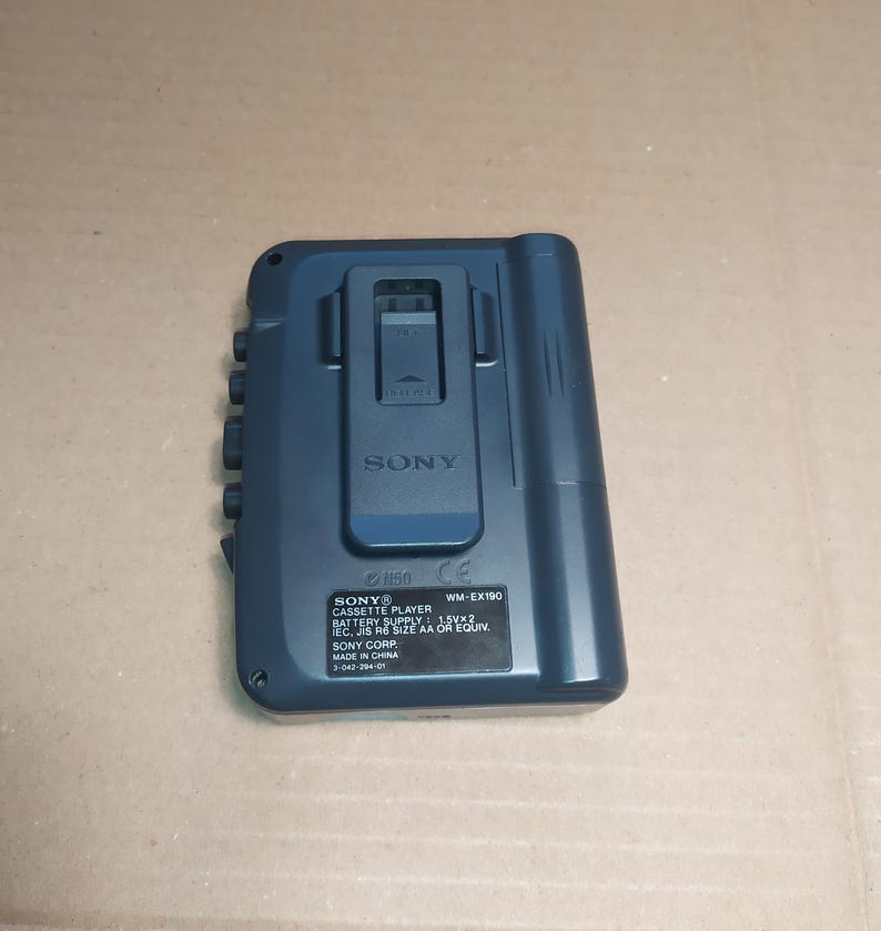 May include: A blue Sony WM-EX190 cassette player with a black belt clip. The player has a CE mark and the text "SONY CASSETTE PLAYER BATTERY SUPPLY 1.5V x 2 EC, JIS R6 SIZE AA OR EQUIV. SONY CORP. MADE IN CHINA 3-042-294-01" printed on the back.