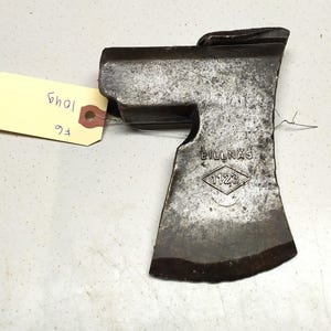 Op de afbeelding: Een vintage bijlkop met een versleten, donkergrijze afwerking. De bijlkop heeft een ruitvormig logo met de tekst "BILLNAS 1123".