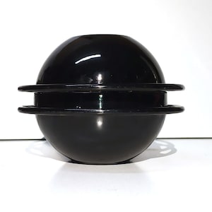 May include: A black ceramic bowl with a smooth, glossy finish. The bowl is stacked on top of a slightly smaller black ceramic bowl. The bowls are round and have a slight lip around the edge.