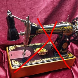 Peut inclure: Une machine à coudre Singer noire et dorée d'époque avec une lampe noire. La machine présente des détails dorés ornés et une base en bois. Le volant et l'aiguille sont visibles, soulignant son design classique.