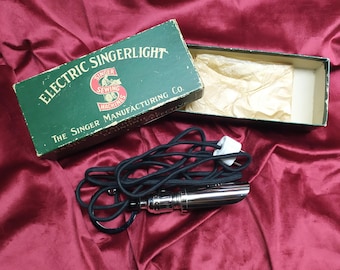 May include: A vintage Singer Electric Singerlight sewing machine light in its original box. The box is green with gold lettering and the light is chrome with a black cord.