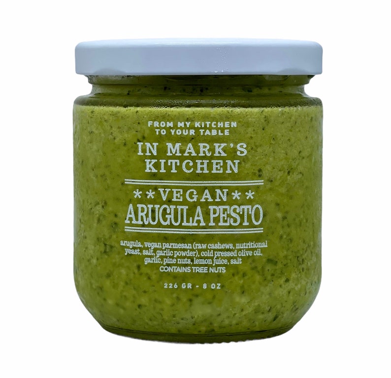 K&ouml;nnte beinhalten: Ein Glas mit gr&uuml;nem Rucola-Pesto und einem wei&szlig;en Etikett mit der Aufschrift "FROM MY KITCHEN TO YOUR TABLE IN MARK'S KITCHEN **VEGAN** ARUGULA PESTO arugula, vegan parmesan (raw cashews, nutritional yeast, salt, garlic powder), cold pressed olive oil, garlic, pine nuts, lemon juice, salt CONTAINS TREE NUTS 226 g - 8 oz"