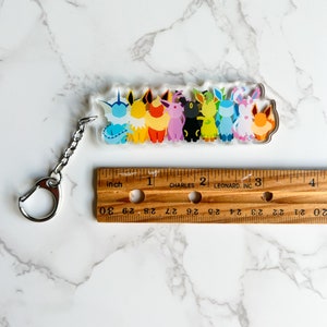 Clear acrylic Eeveelution keychain next to a ruler, showing that the acrylic keychain is roughly 3 inches wide.