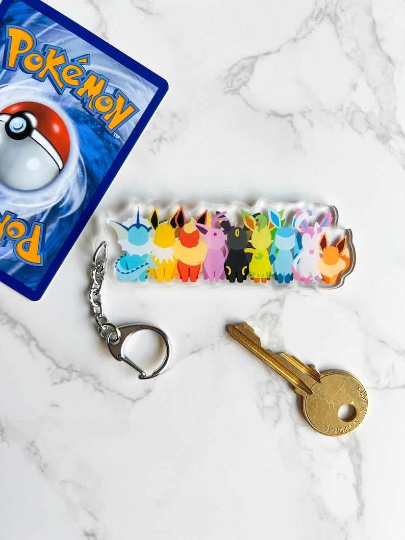 Clear acrylic Eeveelution keychain next to a Pokemon card and a key