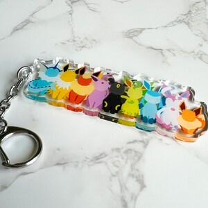 Close up of the Eeveelutions keychain to show the vibrant colors, metal clip on keyring, and durable high quality acrylic material.