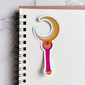 Holographic Moon stick wand sticker on top of a notebook. This sticker is the ideal size for journals, planners, and notebooks.
