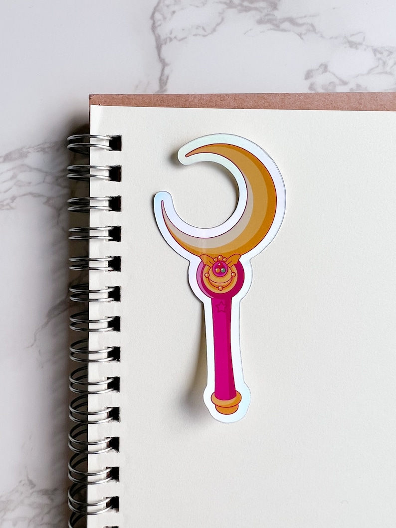 Holographic Moon stick wand sticker on top of a notebook. This sticker is the ideal size for journals, planners, and notebooks.