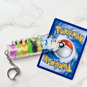 Shiny Eeveelution keychain on top of a Pokemon card. Shiny Pokemons have a different look and are rare variants of their normal counterparts. Perfect for fans of the trading cards, video games, or anime