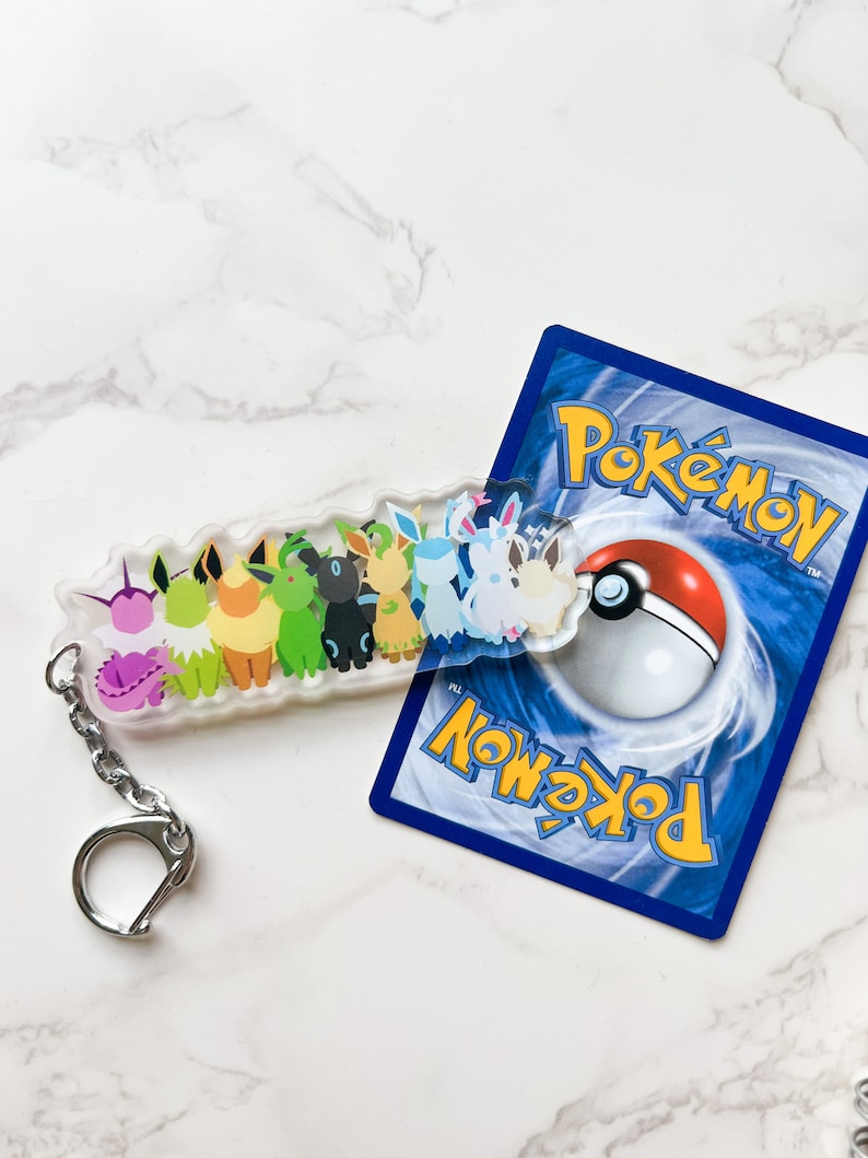 Shiny Eeveelution keychain on top of a Pokemon card. Shiny Pokemons have a different look and are rare variants of their normal counterparts. Perfect for fans of the trading cards, video games, or anime