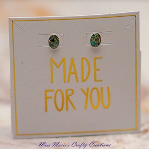 Op de afbeelding: Een paar oorringen van iriserende opaal op een witte kaart met gouden letters die "MADE FOR YOU" zeggen.