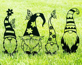 May include: Four black metal garden gnomes with butterfly accents. The gnomes are standing in a grassy area.