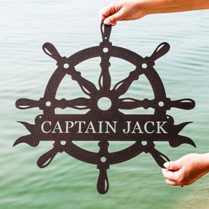 May include: A brown metal ship's wheel with eight spokes and a banner that reads "CAPTAIN JACK".