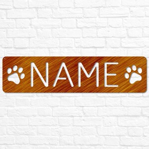 May include: A brown wooden sign with the word "NAME" cut out in white. The sign has two white paw prints on either side of the word.