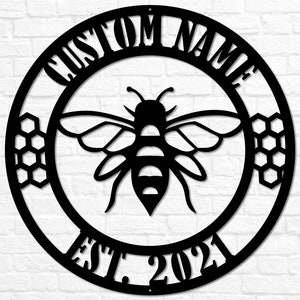 May include: Black metal circle sign with a bee and honeycomb design. The sign says "Custom Name Est. 2021".