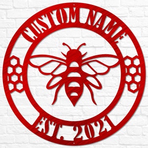May include: Red metal circle with the text "CUSTOM NAME EST. 2021" around the edge. A stylized bee with honeycomb designs is in the center.