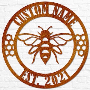 May include: A round, brown metal sign with a bee and honeycomb design. The sign says "Custom Name Est. 2021".