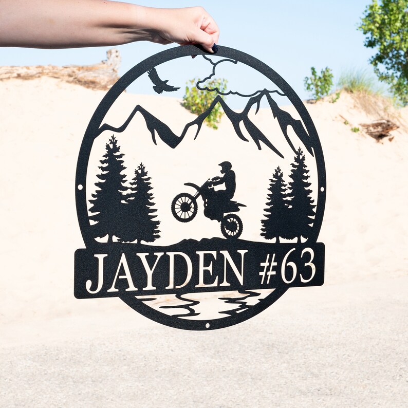 Puede incluir: Se&ntilde;al de metal negro con una escena de monta&ntilde;a, un piloto de motocross y el nombre "JAYDEN #63".