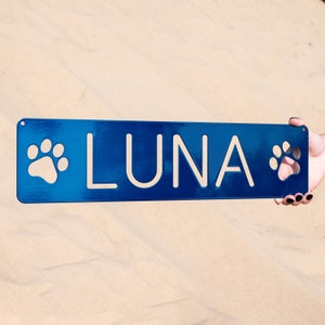 May include: A blue metal sign with white paw prints on either side and the name "LUNA" in white lettering.