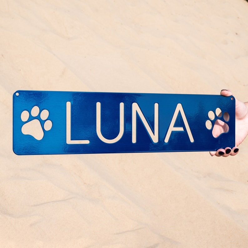 May include: A blue metal sign with white paw prints on either side and the name "LUNA" in white lettering.