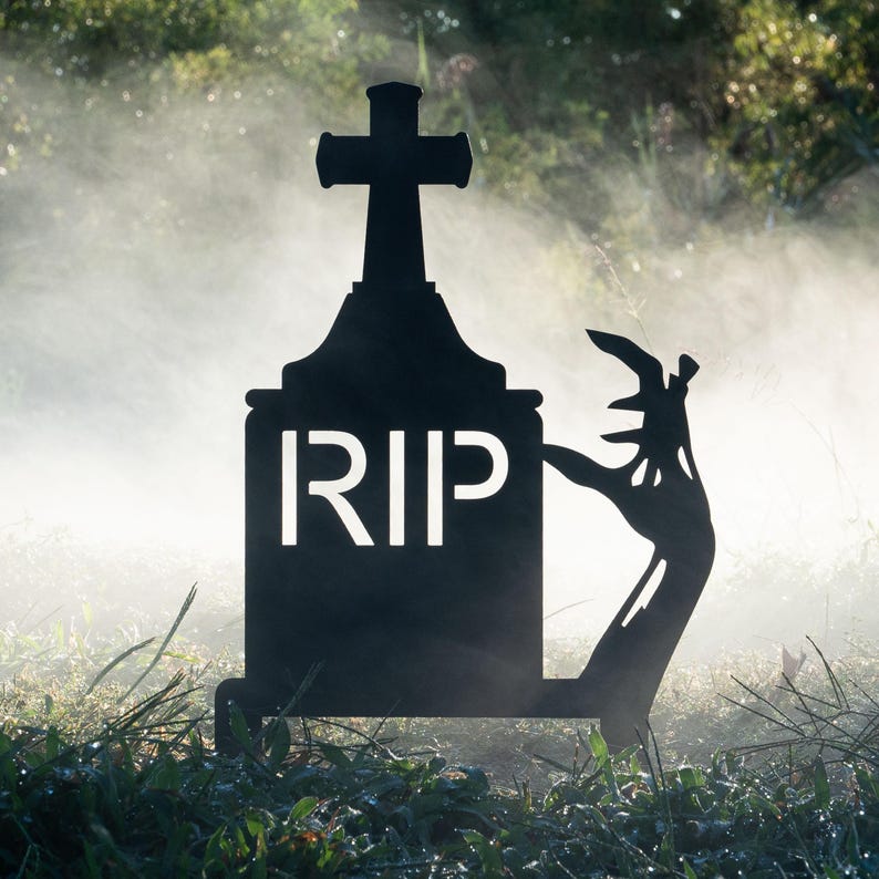 May include: Black metal tombstone silhouette with the letters "RIP" and a cross on top. A zombie hand is reaching out from the ground, creating a spooky Halloween decoration.