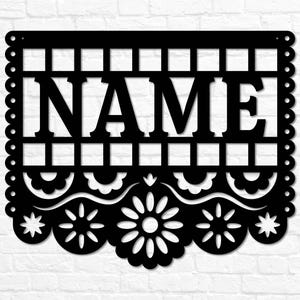 May include: Black metal sign featuring the word "NAME" in capital letters. The sign has a decorative border with scalloped edges and floral cutouts. The background is a white brick wall.