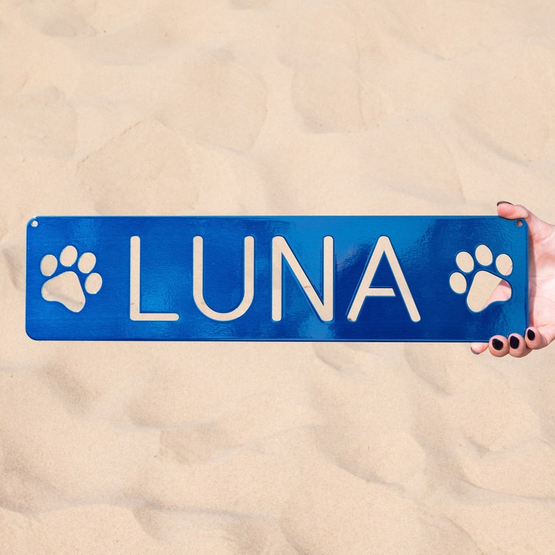 May include: A blue metal sign with paw prints on either side and the name "LUNA" in white lettering.