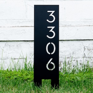 May include: Black metal house number sign with white numbers 3306. The sign is standing in a grassy area.