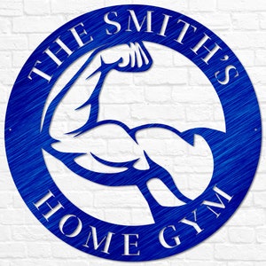 K&ouml;nnte beinhalten: Ein blaues rundes Schild aus Metall mit dem Text "THE SMITH'S HOME GYM" in wei&szlig;en Buchstaben. Im Zentrum des Kreises befindet sich eine wei&szlig;e Silhouette eines Bizepses.
