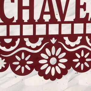 May include: A close-up of a burgundy decorative cutout with the word "CHAVE" at the top. The cutout features a repeating pattern of squares and floral designs. The background is a white, textured surface.