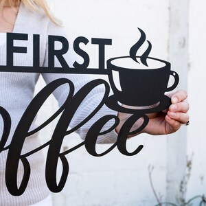 May include: Black metal wall decor with the words "First Coffee" in a stylized font. A black silhouette of a coffee cup with steam rising from it is above the word "Coffee".