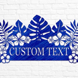 Puede incluir: Arte de pared de metal azul con hojas y flores tropicales y una pancarta de texto personalizable que dice "CUSTOM TEXT".