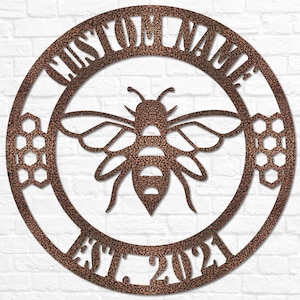May include: A circular metal sign with a rustic brown finish. The sign features a bee with honeycomb designs and the text "CUSTOM NAME EST. 2023".