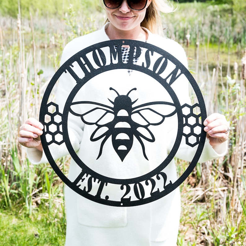 May include: Black metal sign with a bee and honeycomb design. The sign reads "Thompson Est. 2022".