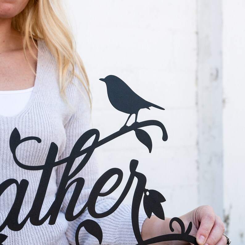 May include: Black metal wall art featuring the word "gather" in a stylised script font. A small bird silhouette sits on a branch with leaves.