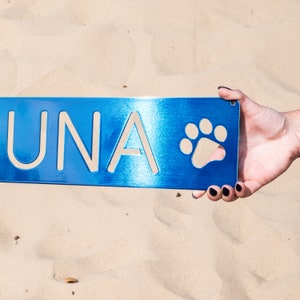 May include: A blue metal sign with the name "UNA" and a paw print in white.