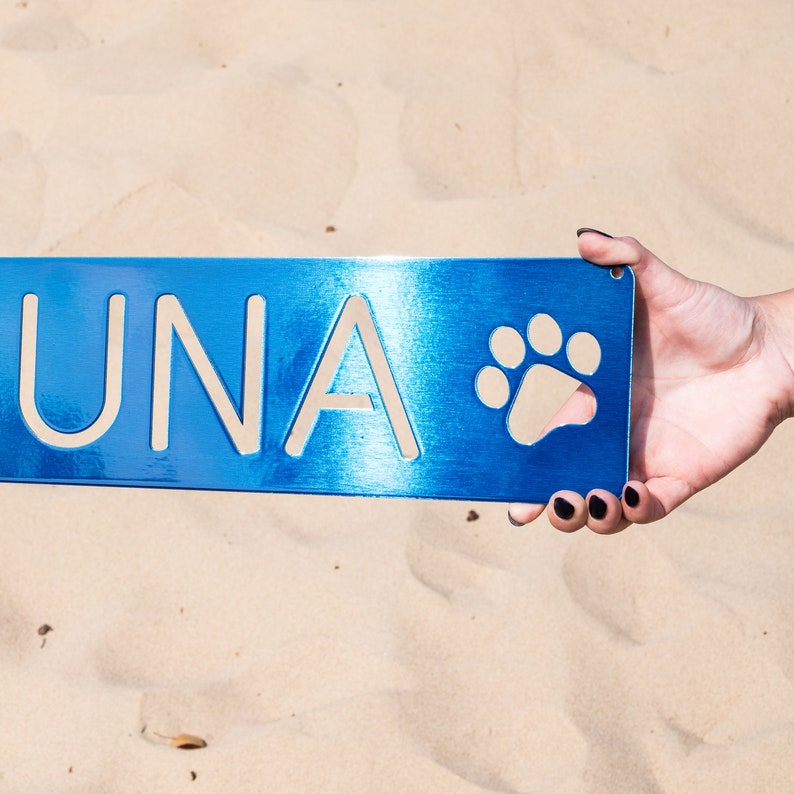 May include: A blue metal sign with the name "UNA" and a paw print in white.