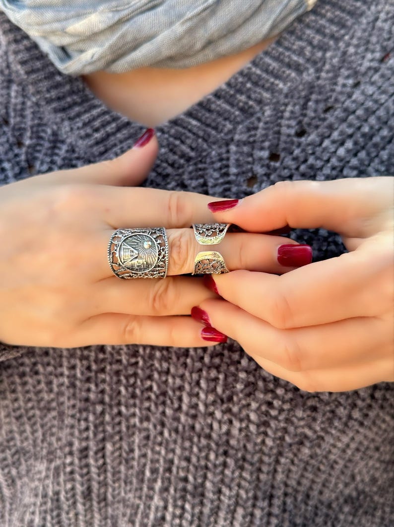 May include: Close-up of three silver rings with intricate designs. The rings are worn on the fingers. The nails are painted a deep red. The rings have detailed patterns, including a rectangular ring with a detailed design.