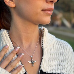 May include: A silver necklace with a winged ankh pendant. The ankh is a symbol of life in ancient Egyptian culture.