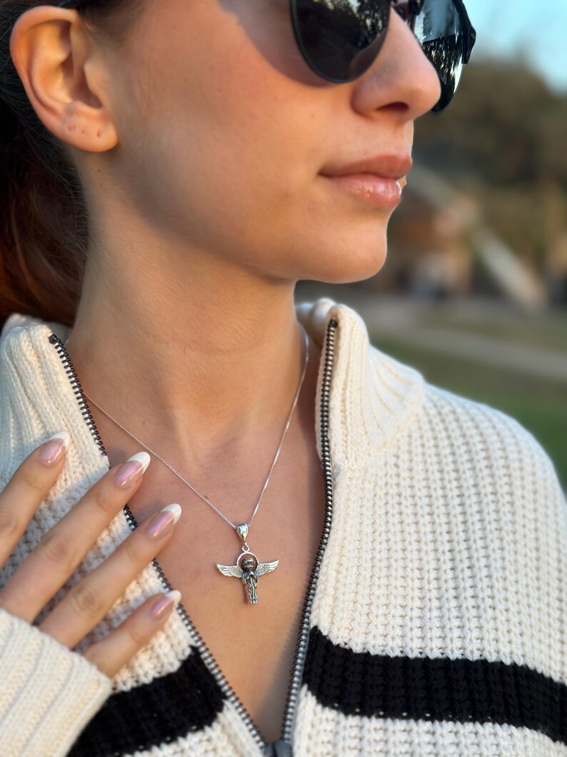 May include: A silver necklace with a winged ankh pendant. The ankh is a symbol of life in ancient Egyptian culture.