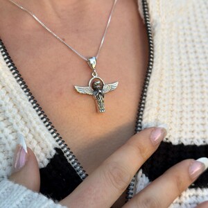 May include: A silver chain necklace with a pendant featuring a detailed angel with outstretched wings. The angel is holding a sphere in its hands.