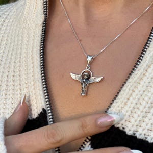 May include: A silver chain necklace with a silver angel pendant. The angel has wings and is holding a small orb in its hands.