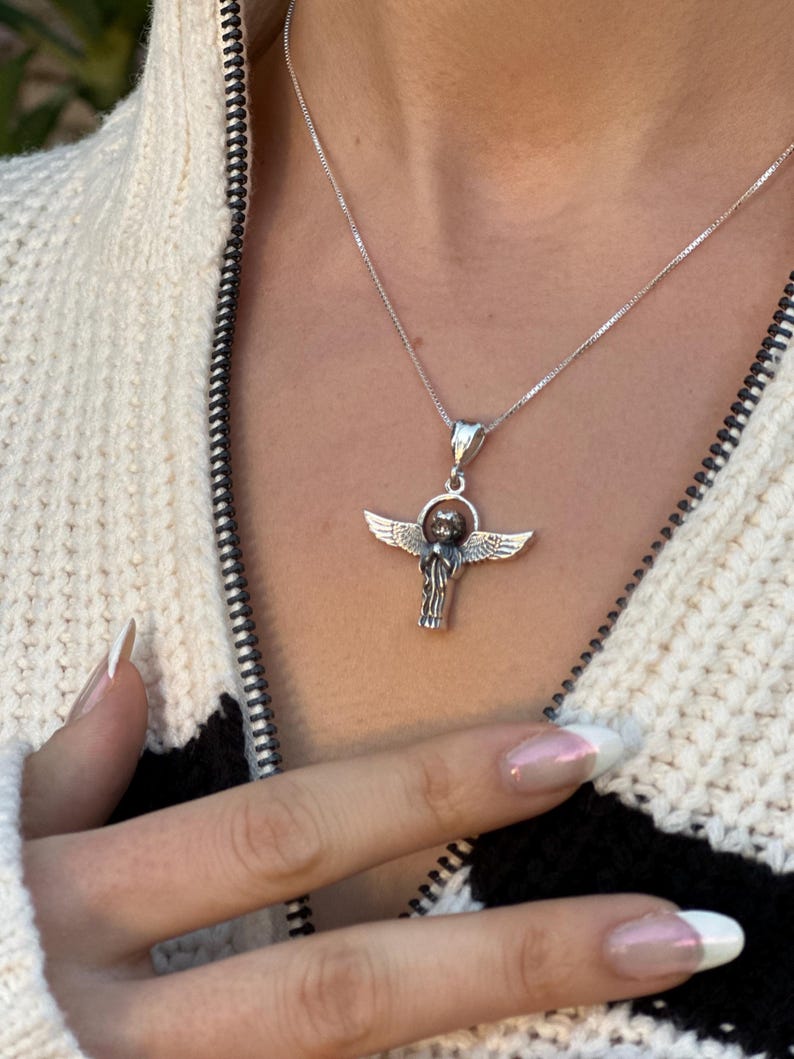 May include: A silver chain necklace with a silver angel pendant. The angel has wings and is holding a small orb in its hands.