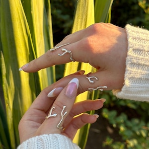 May include: Two silver rings shaped like branches with multiple prongs. The rings are worn on the fingers of two hands.