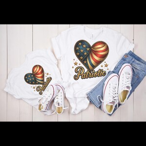 May include: White t-shirts with a heart-shaped design featuring the American flag and the word "Patriotic" in gold script. The shirts are paired with blue jeans and white sneakers with red accents. The design includes stars and stripes.