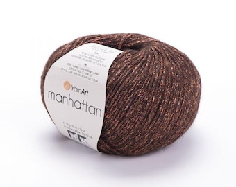 May include: A ball of dark brown YarnArt Manhattan yarn with metallic copper-colored fibers woven throughout. A white paper label is wrapped around the center, featuring the brand name, product name, and technical specifications in 50g/1.76 oz.