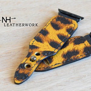 May include: Two leopard print Apple Watch bands with black stitching and metal clasps. The bands are made of leather and have a yellow and brown color scheme.