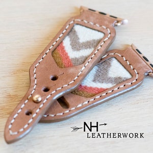 May include: Two brown leather Apple Watch bands with a white and gray chevron pattern and a red accent. The bands are stitched with white thread and have a gold metal buckle. The bands are labeled "NH-> LEATHERWORK".