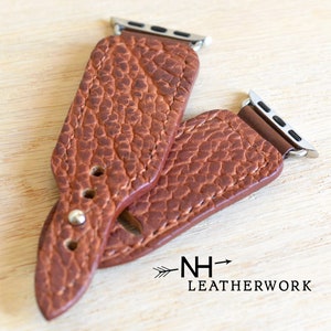 May include: Two brown leather watch bands with silver metal clasps. The bands have a textured, pebbled surface. The bands are stacked on top of each other. The text "NH-> LEATHERWORK" is visible in the lower right corner of the image.