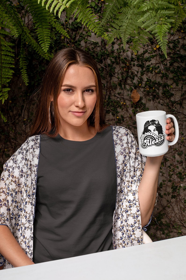 May include: A white ceramic mug with a black and white graphic design featuring a woman's face and the text "Little bit Alexis".